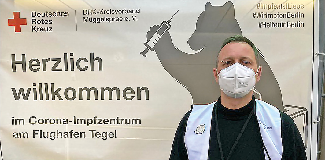 Mann vor Plakat des Impfzentrums Tegel