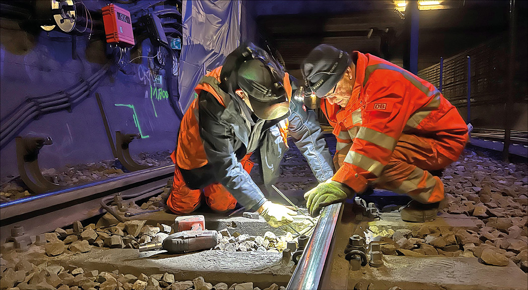 Bauarbeiter mit Schutzausrüstung flexen an einer S-Bahnschiene im Tunnel