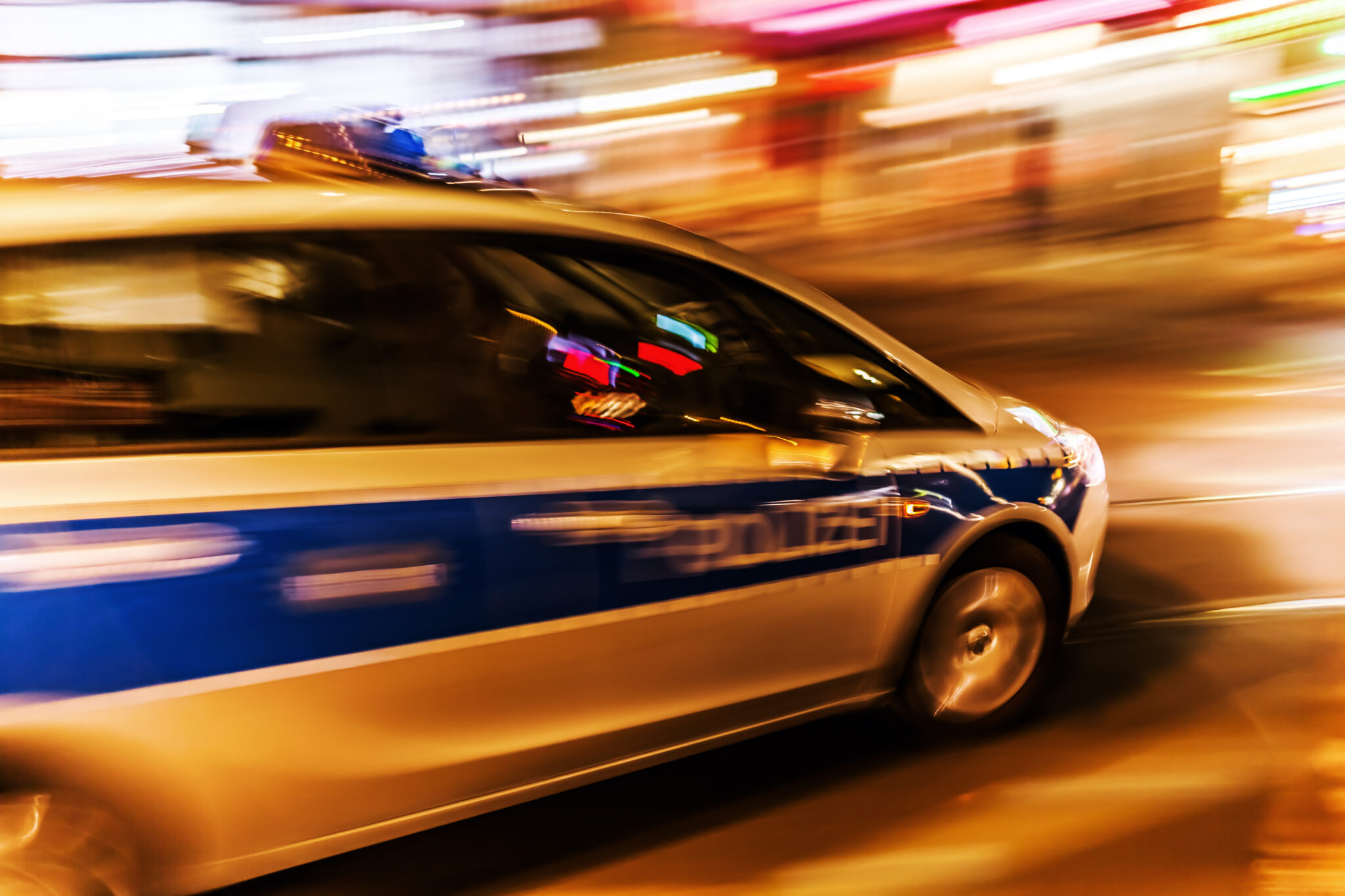 Ein Polizeiauto fährt durch die Nacht auf einer beleuchteten Straße.