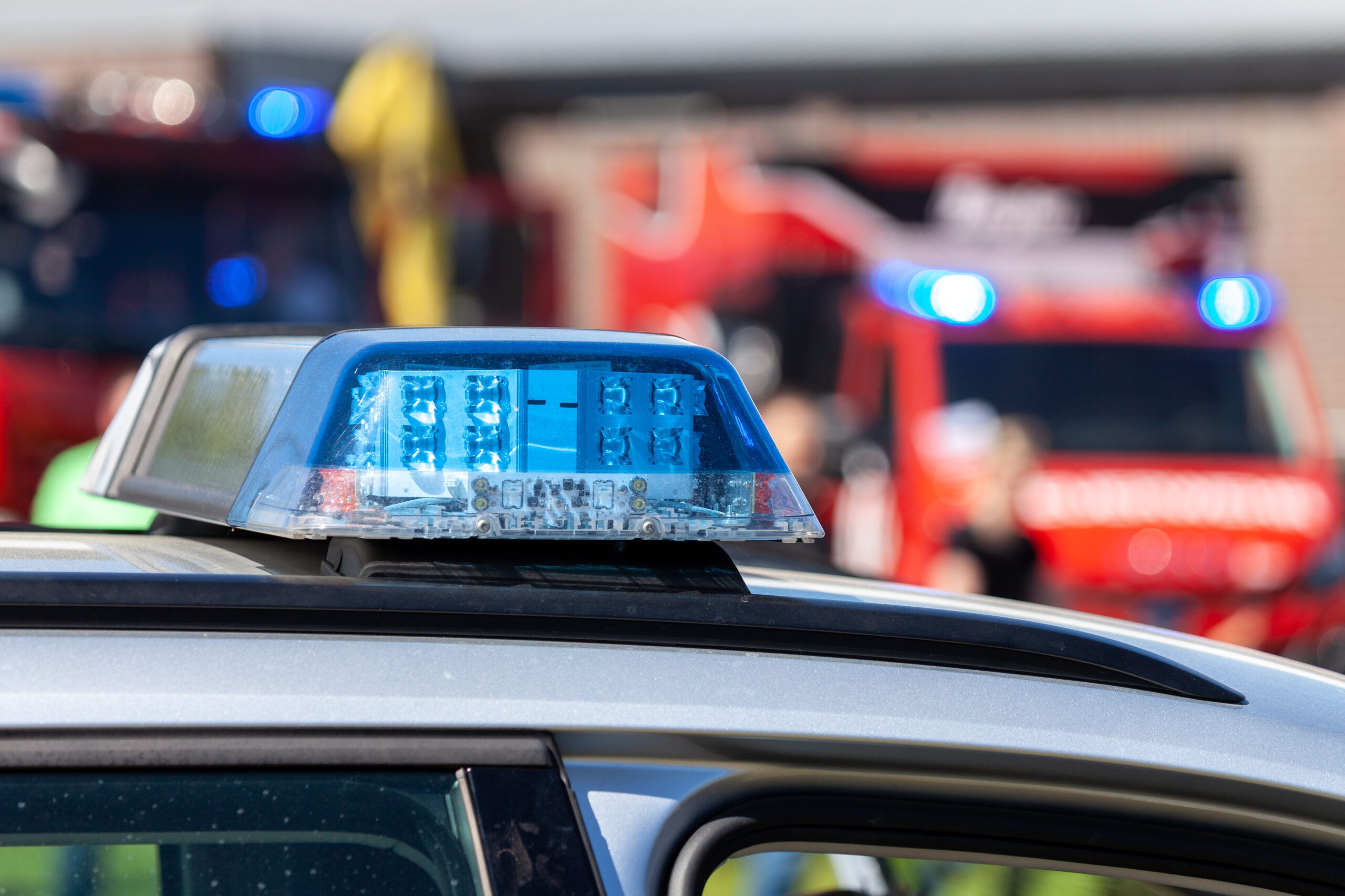 Im Vordergrund sieht man das Dach-Blaulicht eines Polizeiautos, im Hintergrund ein Feuerwehrfahrzeug.