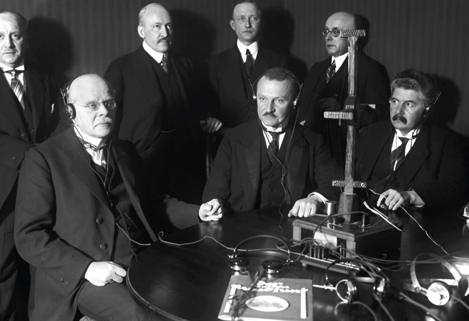 Eine Schwarz-Weiß-Aufnahme zeigt eine Gruppe Männer vor einem historischen Gerät.