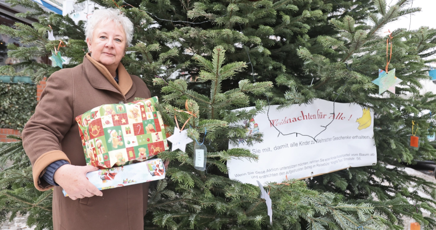 Eine Frau steht mit verpackten Geschenken vor einem Tannenbaum.