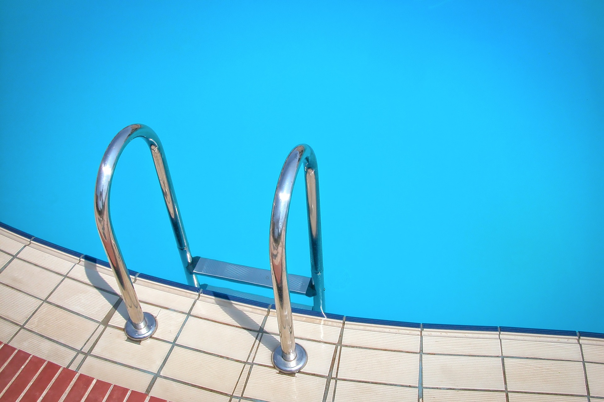 Eine metallene Leiter, die vom Beckenrand ins Wasser eines Pools führt