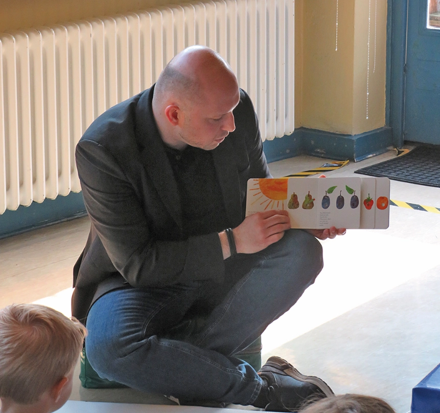 Ein Mann hält einer Gruppe Kinder ein Lesebuch so hin, dass sie die Bilder sehen können.