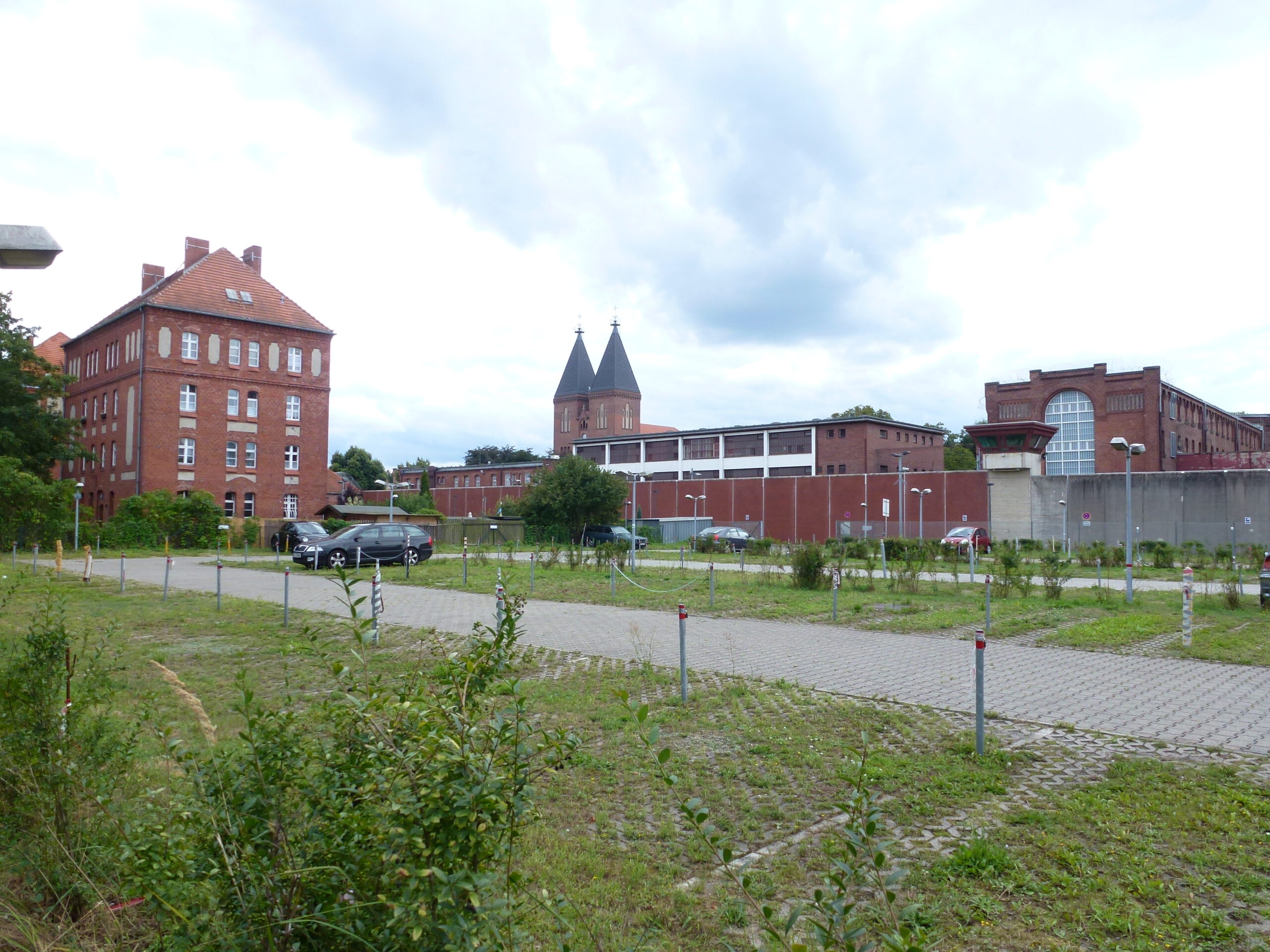 Außenansicht der JVA Tegel, im Vordergrund Wiese, dahinter die roten Backsteingebäude.