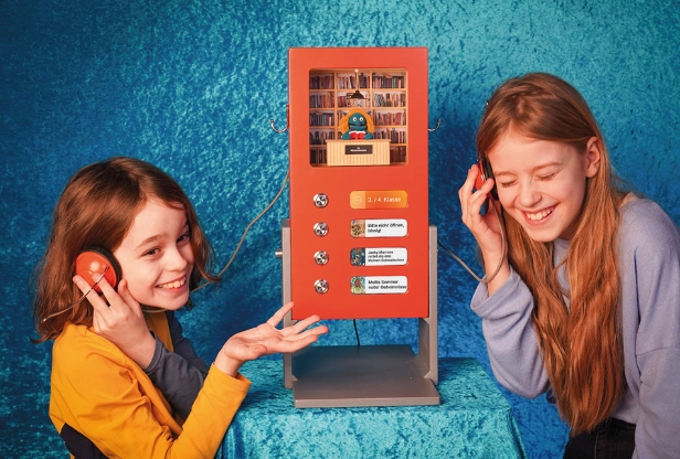 Zwei Mädchen stehen an einem roten Automaten, dem Buchfindomaten.