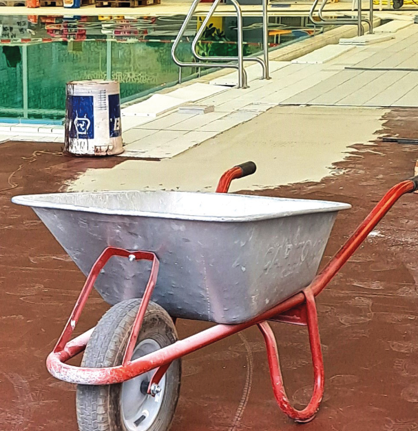 Baustelle im Schwimmbad: Im Vordergrund eine Schubkarre, dahinter der Beckenrand.