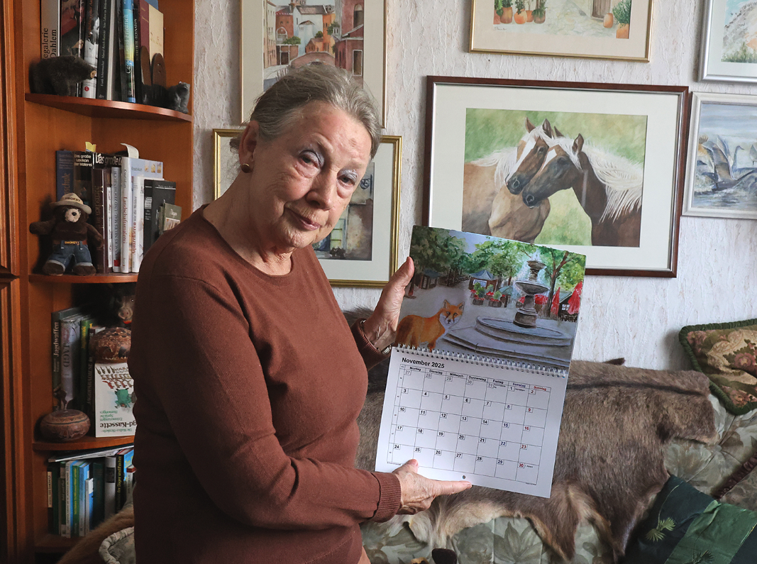 Eine Frau zeigt einen aufgeblätterten Wandkalender in die Kamera.