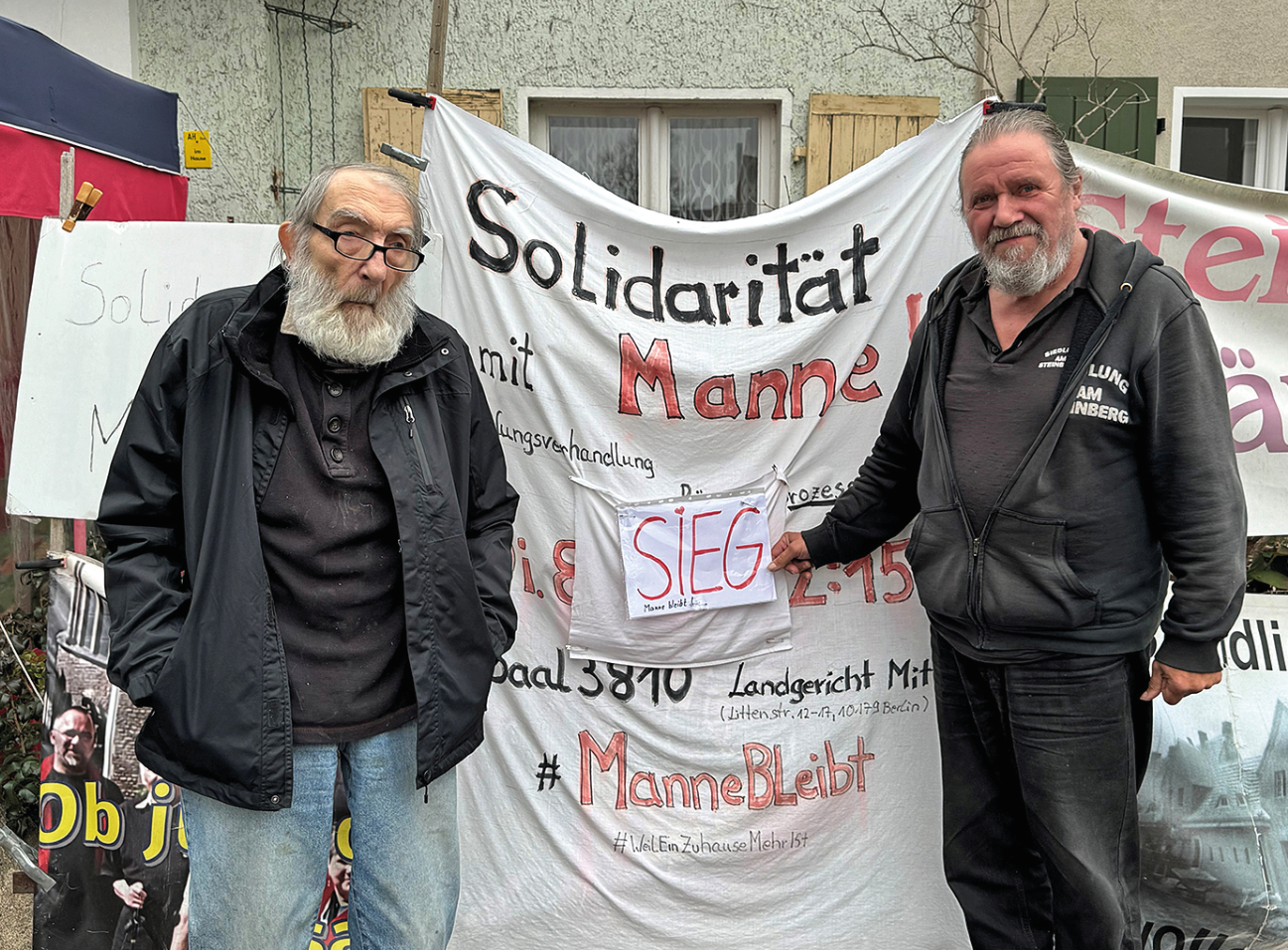 Zwei Männer vor einem Protest-Plakat, auf dem "Solidarität mit Manne" zu lesen ist.