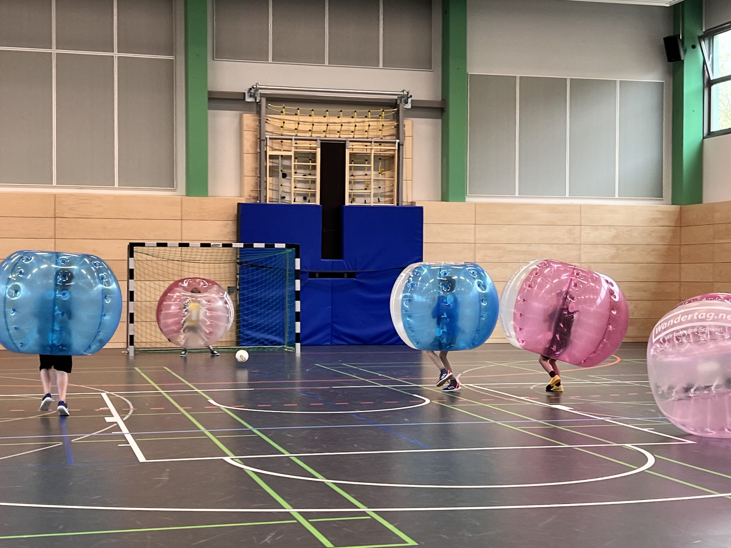 Eine Sporthalle mit Blick auf ein Handball-Tor: Davor Menschen in großen Bubble-Soccer-Bällen