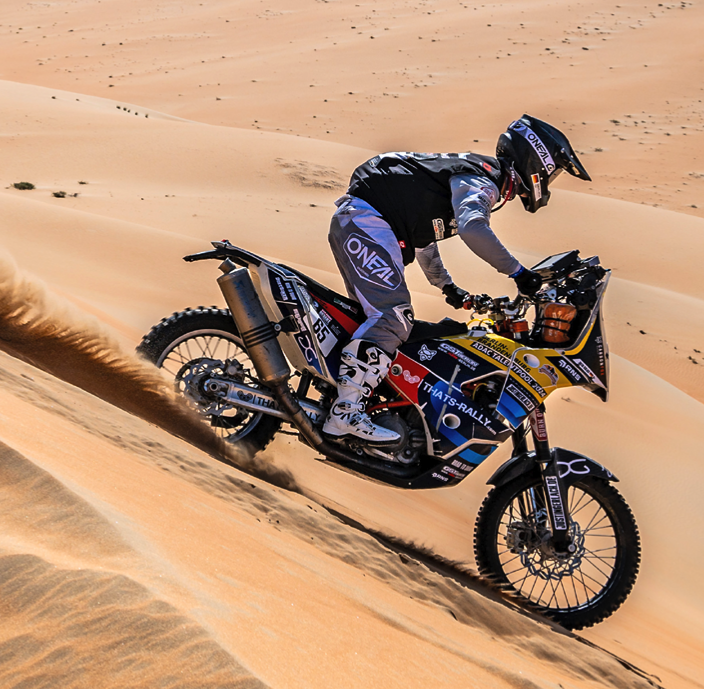 Ein Motorrad-Cross-Fahrer fährt eine Sanddüne in einer Wüste hinunter.