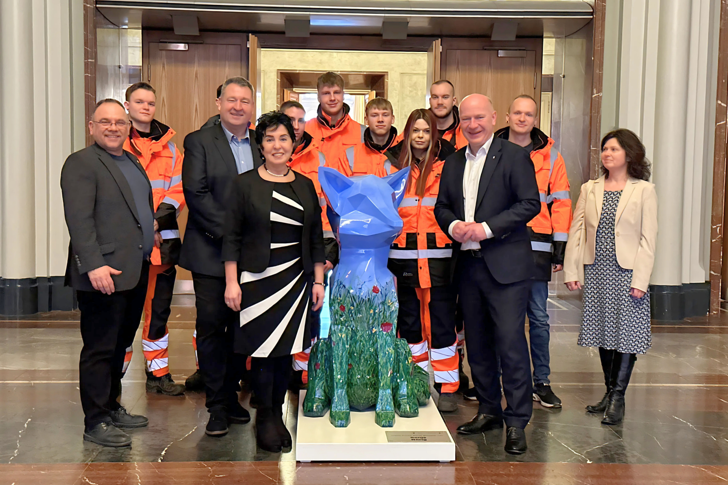 Die Skulptur eines blau-grünen Fuchses, umringt von einer Gruppe Menschen.