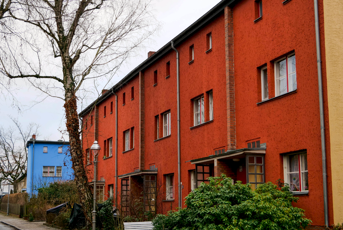 Eine rote Hausfassade, im Hintergrund eine weitere, aber blaue.