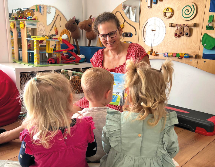 Eine Frau sitzt mit 3 Kindern in einem Spielzimmer