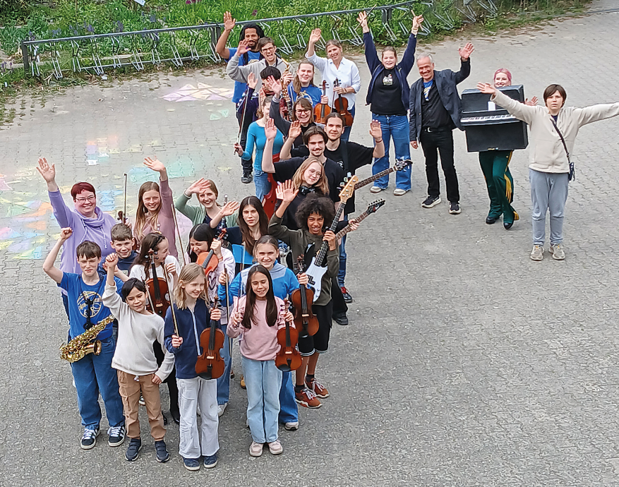 Viele Kinder mit Musikinstrumenten auf einem Schulhof, die einen Notenschlüssel bilden.