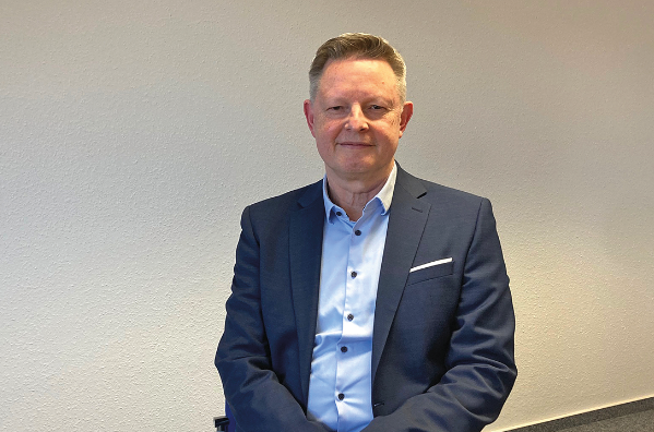 Ein Mann sitzt auf einer Tischkante in einem Büro und schaut in die Kamera.