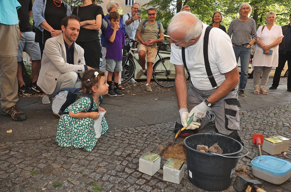 ein Mann setzt Stolpersteine in den Gehweg ein, ein Mädchen schaut zu