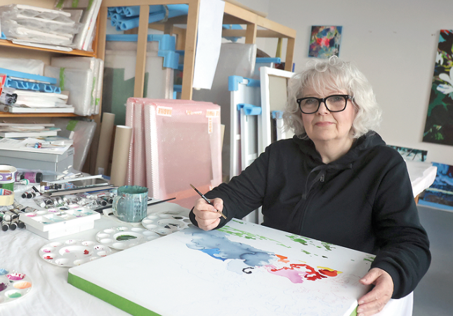 Eine Frau sitzt in einem Atelier an einem Schreibtisch mit Kunst