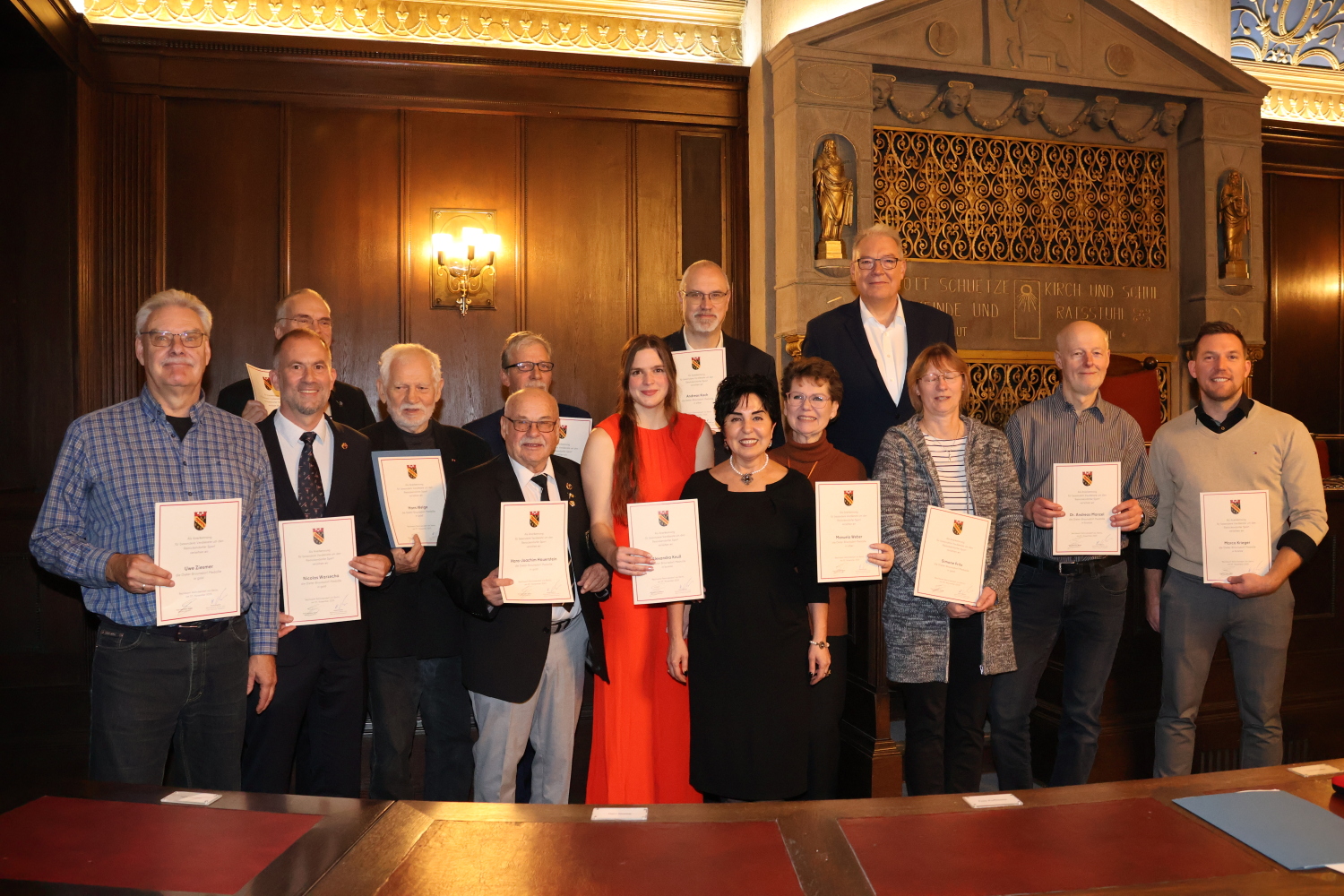 Eine Gruppe von Menschne in einem Saal. Sie halten Urkunden vor sich.