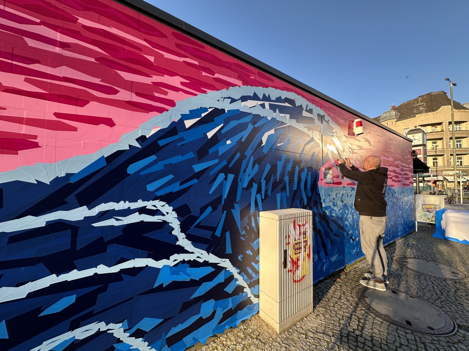 Ein Mann arbeitet an einer Fassadengestaltung: Einer blauen Welle vor pinkem Hintergrund.