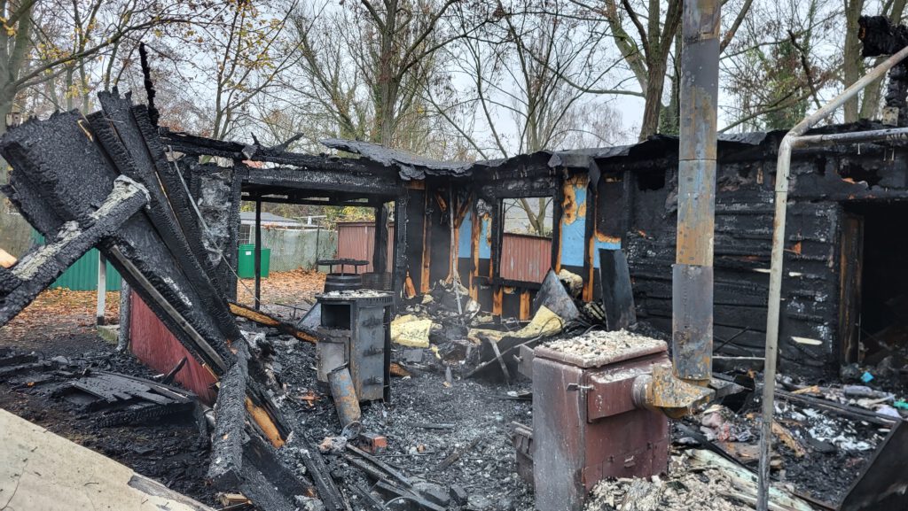 Ein von einem Brand verwüstetes Gebäude, im Hintergrund kahle Bäume.