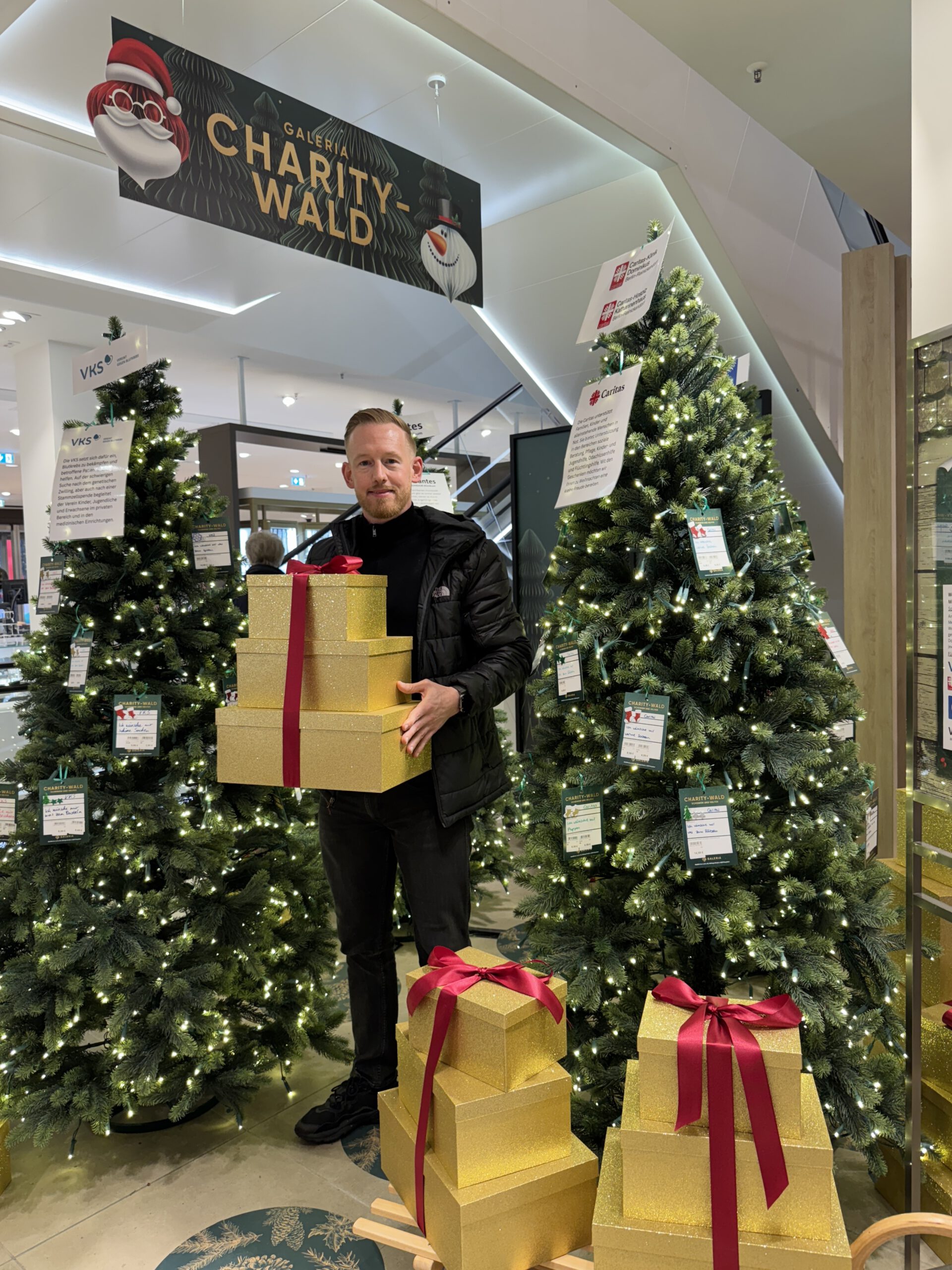 Ein Mann, flankiert von Weihnachtsbäumen, mit goldenen Geschenkpaketen