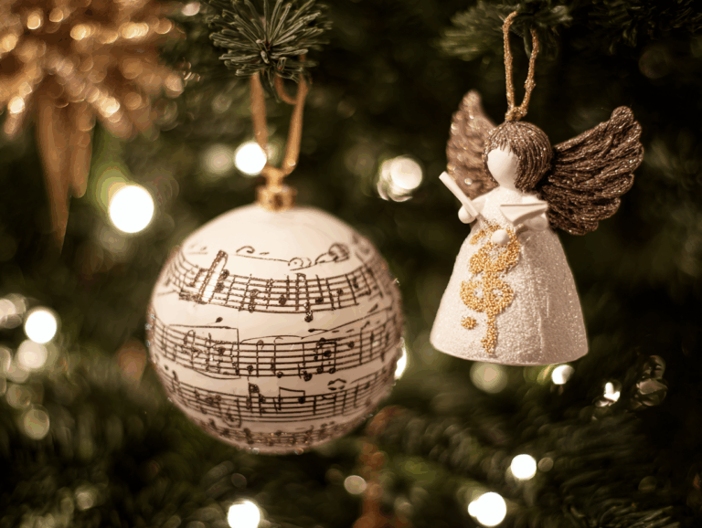 Blick in Weihnachtsbaumzweige: Zu sehen sind eine Christbaumkugeln, die mit Notenlinien dekoriert ist, daneben eine Engelsfigur als Anhänger