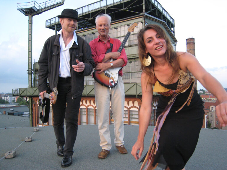 Eine Frau und zwei Männer mit Musikinstrumenten vor einem Gebäude.