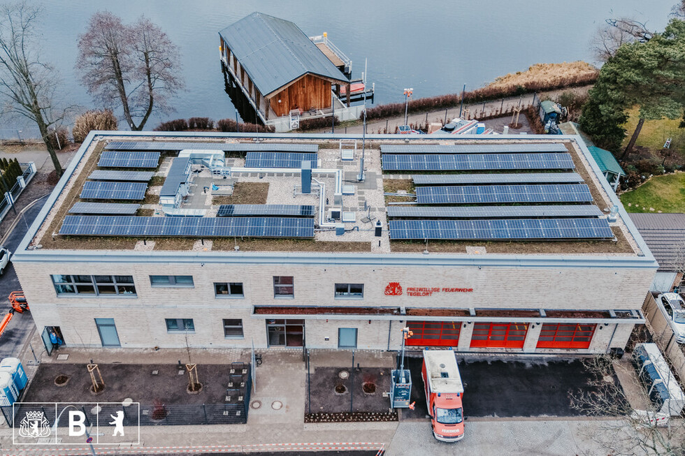 Luftaufnahme eines großen Gebäudes mit Feuerwehr-Toren. Auf dem Dach sieht man Photovoltaik-Anlagen.