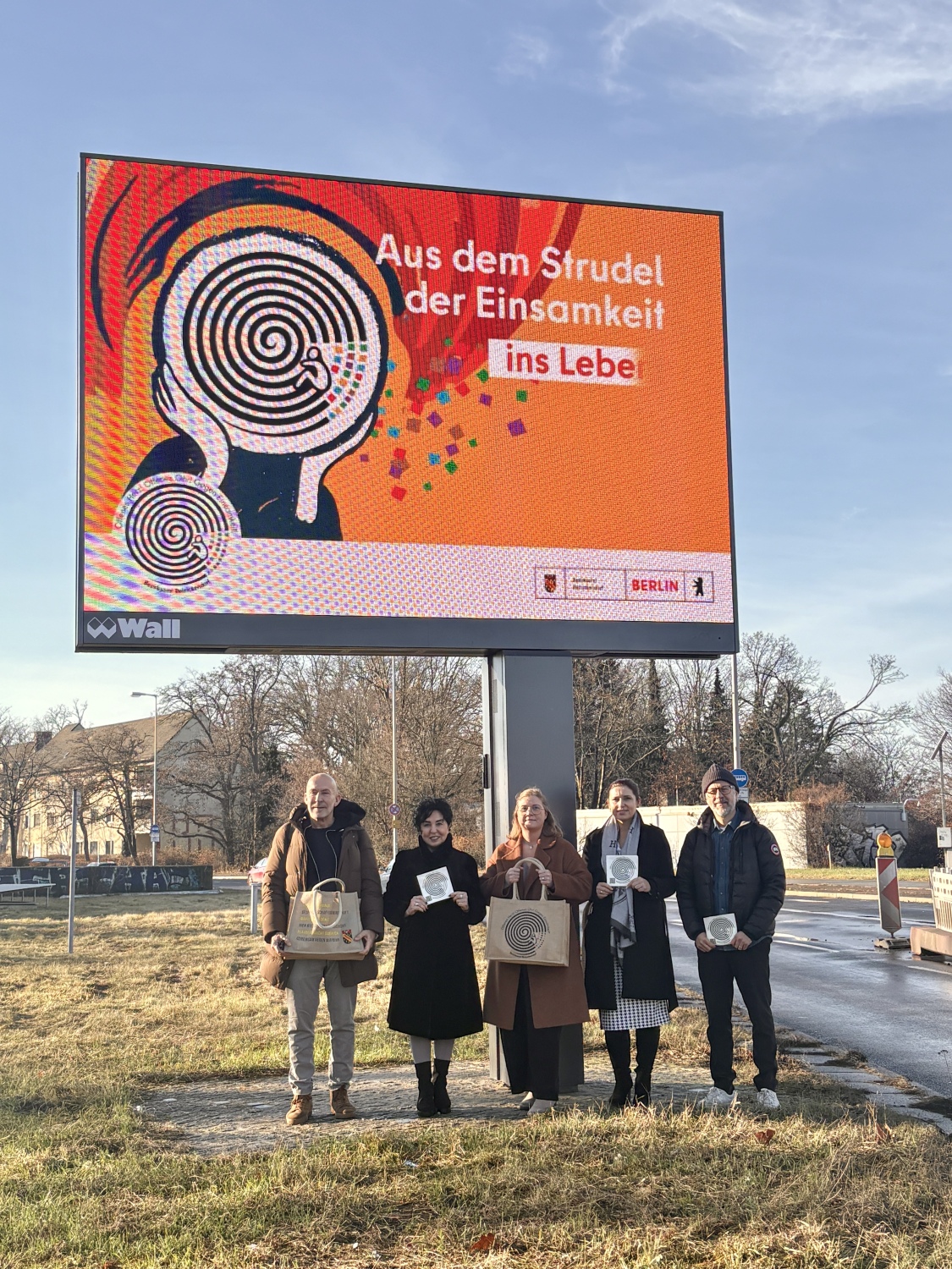 Fünf Menschen vor einem großen digitalen Reklameschild mit einer Anti-Einsamkeitskampagne