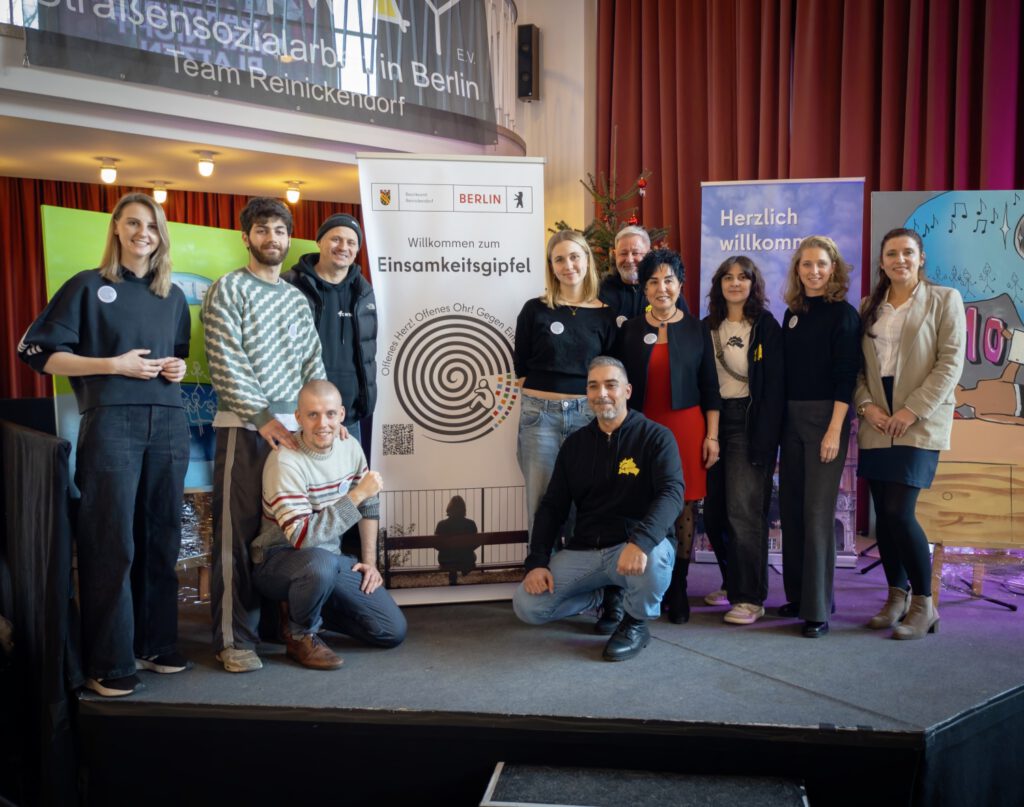 Mehrere Menschen stehen und hocken für eine Gruppenaufnahme, in ihrer Mitte ein Roll-up-Banner