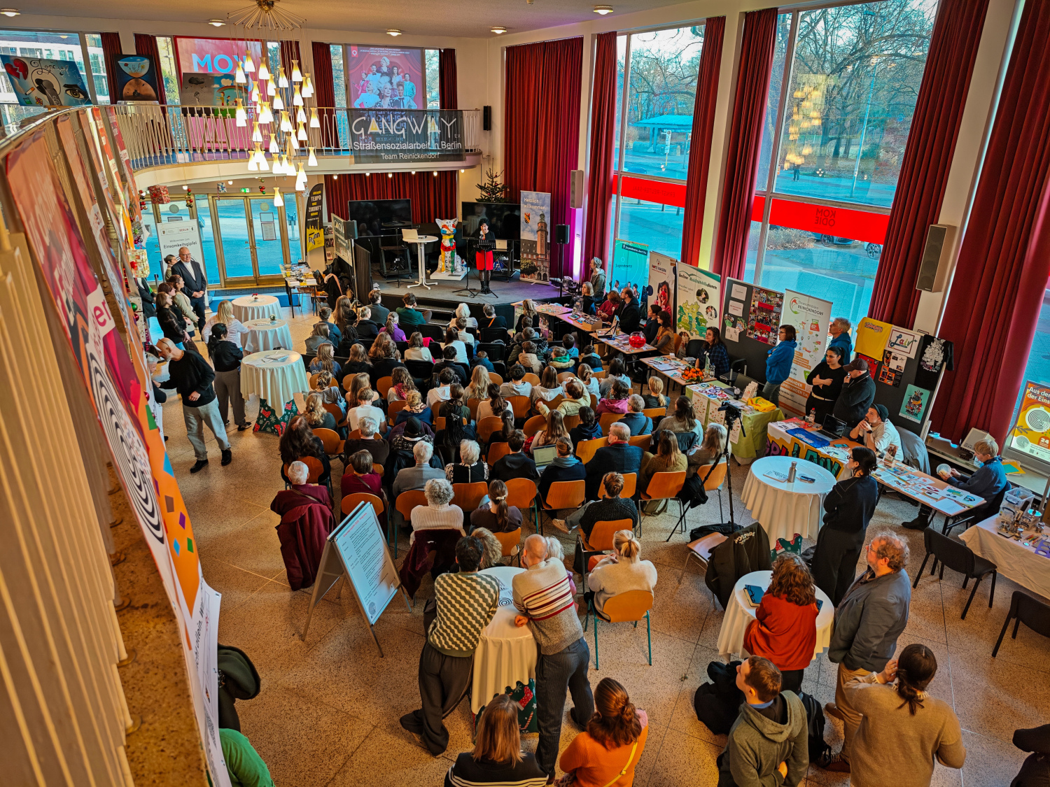 Blick von einem erhöhten Standpunkt in einen großen Saal - von hinten Richtung eines großen Publikums, das auf Stühlen vor einer Bühne sitzt