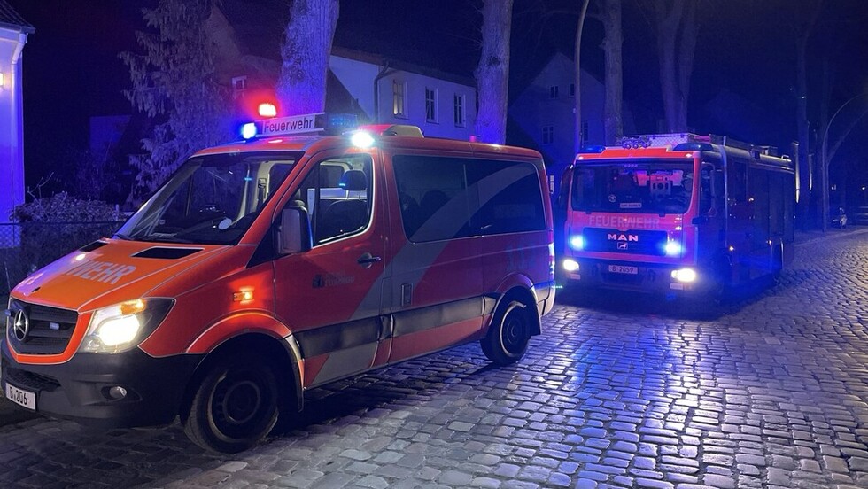 Zwie Einsatzfahrzeuge der Feuerwehr mit eingeschaltetem Blaulicht auf einer Kopfsteinpflaster-Straße