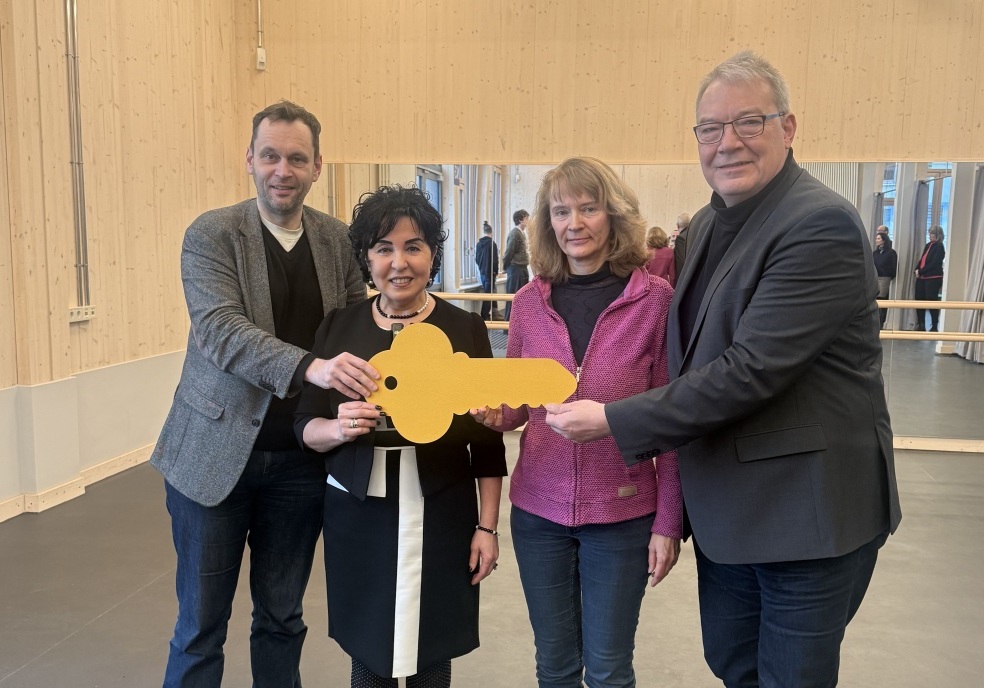 Vier Menschen halten in ihrer Mitte einen übergroßen gelben Schlüssel als Symbol für eine Eröffnung