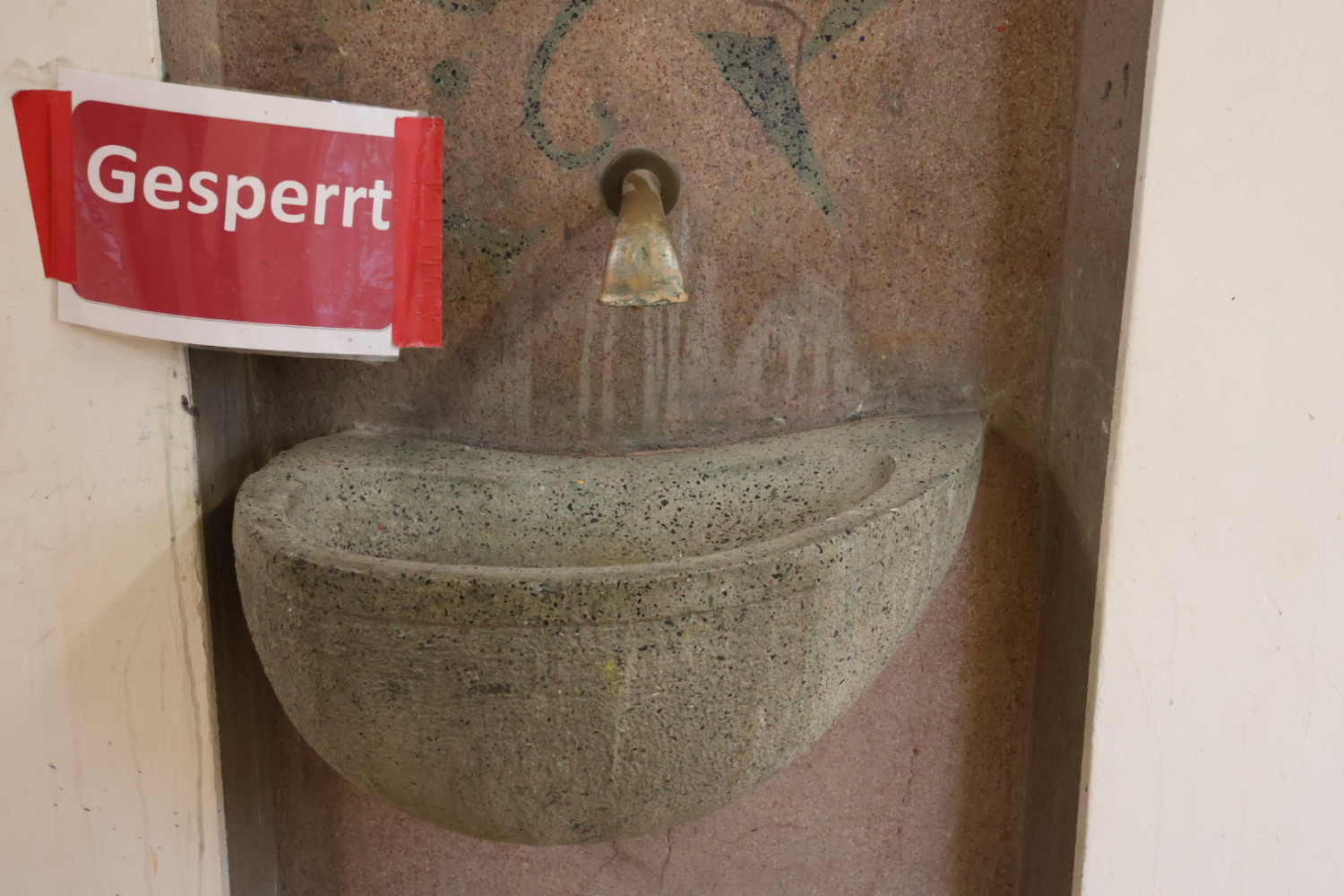 Ein altes Steinwaschbecken an einer Wand mit einem darüberliegenden Hahn. Daneben ein Schild mit der Aufschrift "Gesperrt".