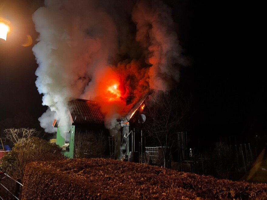 Eine Laube steht in Flammen. Feuer und Rauch schlagen aus dem Dach in den schwarzen Nachthimmel