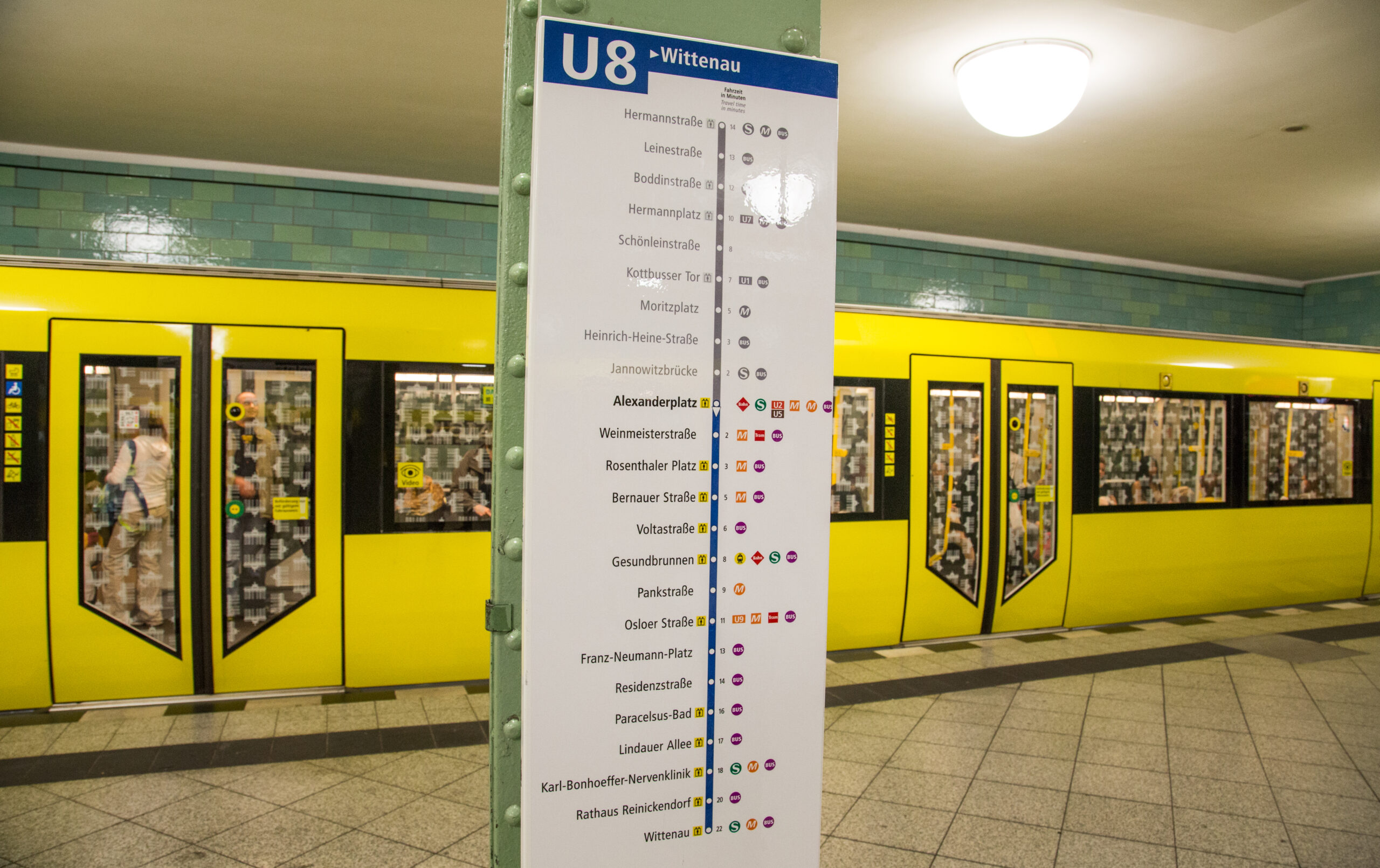 Eine U-Bahn an einem U-Bahn-Gleis in einer Station. Im Vordergrund ein Schild, das über den Verlauf der Linie U8 aufkärt.