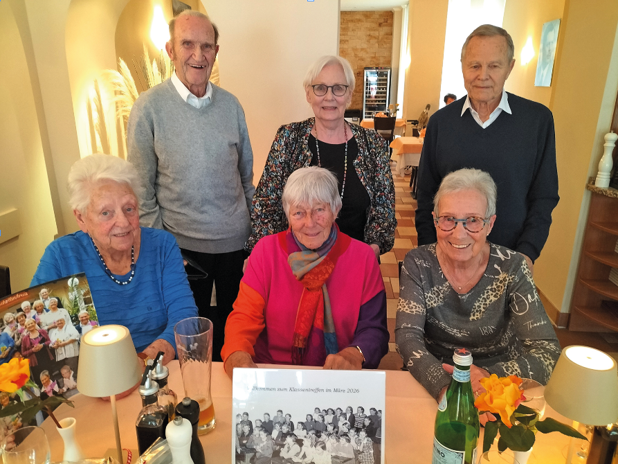 Sechs ältere Menschen hinter dem Foto der Klasse damals