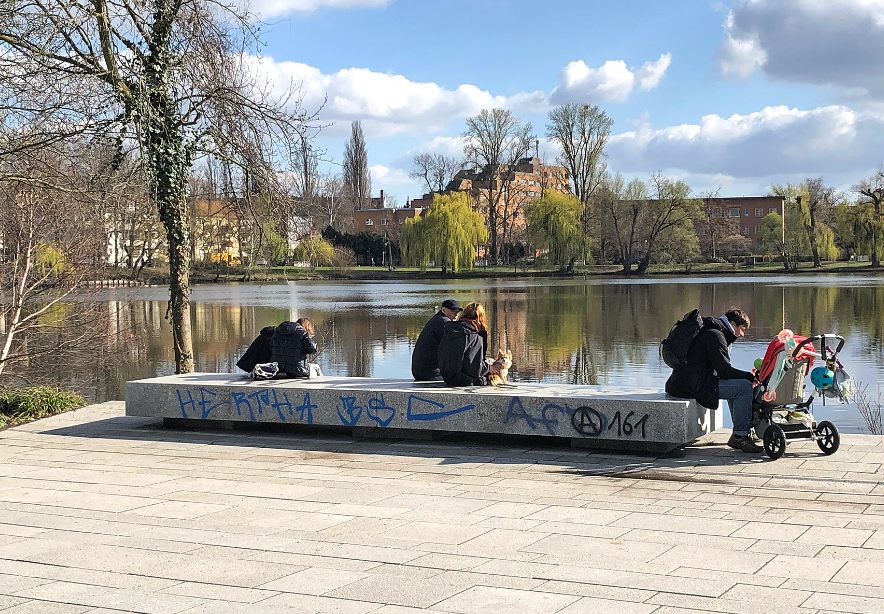 Menschen sitzen am Ufer eines Sees und schauen aufs Wasser