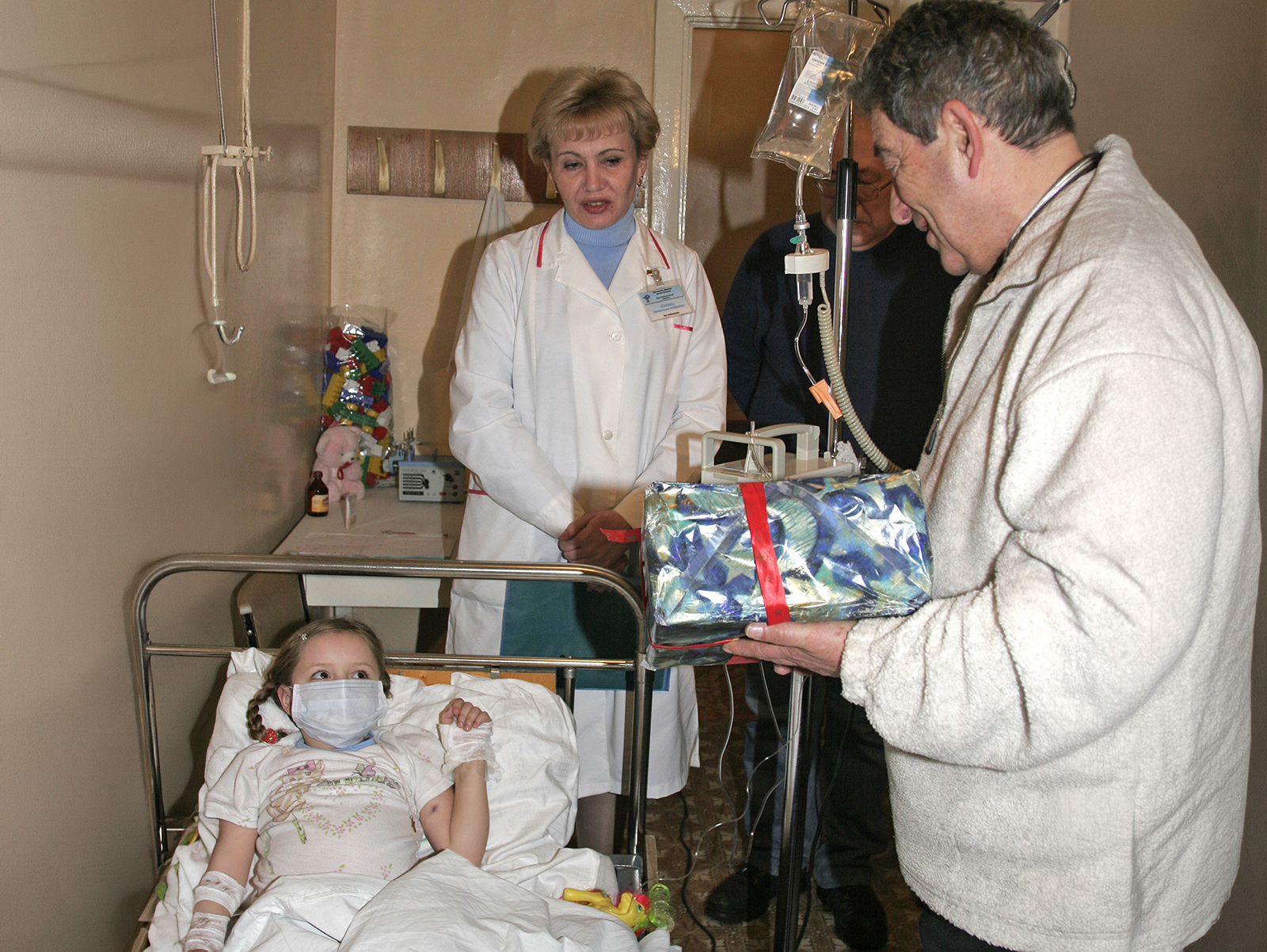Im Krankenzimmer überreicht ein Mann einem Kind ein Geschenk