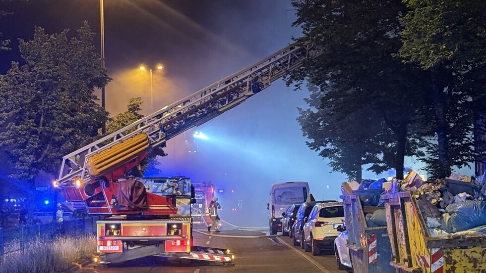 Feuerwehr-Leiterauslieger in einer Straße bei Flutlicht in der Nacht. Viel Rauch ist in der Luft.
